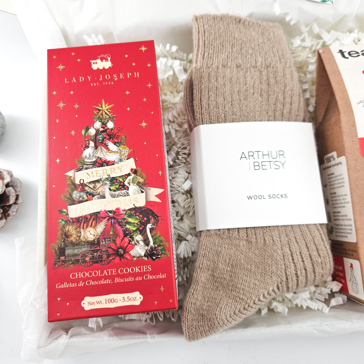 Close-up of Lady Joseph Christmas chocolate biscuits, beige wool socks and Teapigs tea in a cosy Christmas gift box.